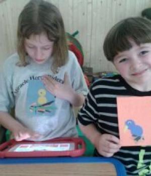 Photo of a girl working on a tablet and a boy proudly displaying his artwork, both patients at Nature's Edge Therapy Center in Rice Lake, WI.