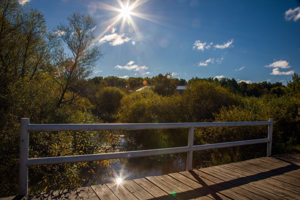 Photo of sun shining over the creek and bridge to Nature's Edge Therapy Center in Rice Lake, WI.